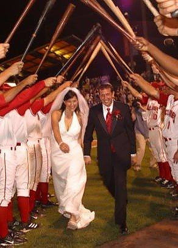 Dave and Carrie Kerpen walking through an arch of crossed baseball bats at their 2006 Brooklyn Cyclones wedding